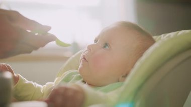 Çok fonksiyonlu bebek koltuğunda oturan ve mutfakta yemek yemeyi reddeden komik bir çocuk. Anne kaşığı tutuyor. Çocukluk, anne ve çocuk. Kapalı