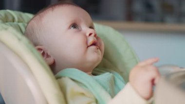 Gülümseyen beyaz çocuğun portresi portresi rahat portatif yemek sandalyesinde oturup anneye bakıyor. Kahverengi gözlü bir çocuğun portresi. Kapalı