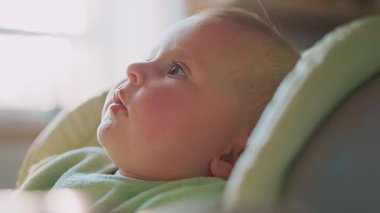 Yemekten sonra yüzüne meyve püresi bulaşmış güzel bir erkek bebeğin portresi. Elinde tepsiyle şezlongda otururken annesine bakan tatlı çocuk. İçeride. - Eve. Annelik