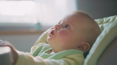 Mutfaktaki çok fonksiyonlu bebek koltuğunda oturan yüzü lekelenmiş bir erkek bebek görüntüsü. Taşınabilir yemek koltuğu. Güvenlik, dikkat. Çocukluk, aile. İçeride. Yakın plan.
