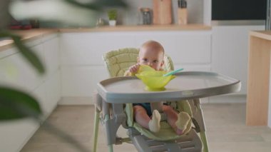 Bebek portresi. Güneş ışığı odasının mutfağında yemek masasında oturuyor. Kap kase yemeye çalışıyorum. Kahvaltıda. - Aile. Çocuklar işte. Yavaş çekim