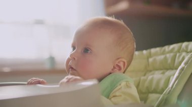 Günışığında, modern bir daire portresi çevreye bakan yüksek sandalyede oturan sevimli bir bebekle yüzleşir. Çocukluk. Kahvaltıda. Yavaş çekim