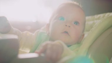 Kapalı bir portre, büyüleyici gülümseyen bir bebek, yüksek bir sandalyeye oturmuş güneş ışığına bakıyor. Çocukluk. Kahvaltıda. Yavaş çekim