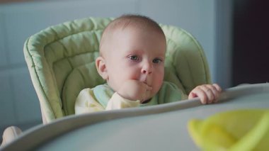 Yemekten sonra yüksek sandalyeyi besleyen portatif sevimli bebek. Yüzü yemek lekesi olan bir çocuk. Modern daireler. Akşam yemeği. Mutfağa. Yavaş çekim