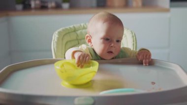 Dairede, bebek yemek yemeye çalışan bir sandalyeyi besliyor. Yemek lekeli yüzü olan mutlu bir çocuk. Yemek. Acıktım. Akşam yemeği. Mutfağa. Yavaş çekim