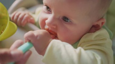 Annenin yüksek sandalyede bebeği beslerken ellerini kapat, çocuk kendini yemeye çalışıyor. Yüzünde yemek lekesi olan bir çocuk. Anne yardım et. Modern apartman mutfağı. Yavaş çekim