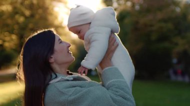 Ormanda yürürken, güzel, yumuşak beyaz giysiler içinde bebeği tutan mutlu bir annenin görüntüsü. Güzel bir annenin kızıyla vakit geçirmekten zevk aldığının portresi. Yeşil ve sarı yapraklı ağaçlar