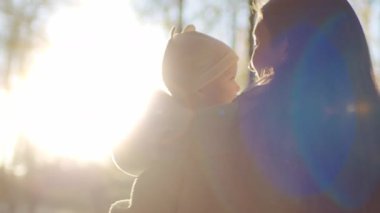 Annesinin ve tatlı bebeğinin sırtına ateş edilmiş. Anne kucağında bebekle ormanda ağaçların bulanık arka planında yürüyor. Güneş ışığı. Açık havada. Sevgi, ilgi