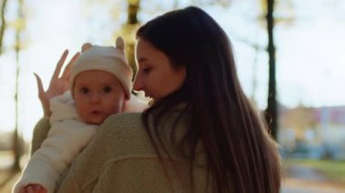 Beyaz tenli güzel bir kadının güzel bir bebeği ellerinde tutması, yürümeye yeni başlayan bir çocuğu öpmesi, anneliğin tadını çıkarması. Sonbahar parkında kameraya bakan sevimli küçük kız. Güneş ışığı. Sevgi, ilgi