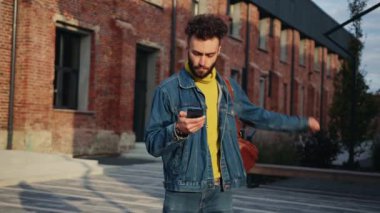 Kot pantolon giymiş, akıllı telefon ekranına bakıp keyfi yerindeyken dans eden kaygısız, beyaz bir genç. Güneşli bir günde şehir sokağında sohbet eden bir adamın görüntüsü.