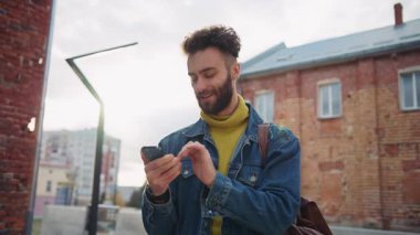 Şık giyinmiş genç bir adamın sokakta akıllı telefondan bir kızla sohbet edişinin görüntüsü. Gülen beyaz adamın sohbetin tadını çıkardığı bir fotoğraf. Mesaj var. İnternet bağımlılığı konsepti. Açık havada. Gündüz vakti. İletişim