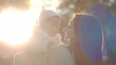 Annenin gün ışığında kızını kollarına aldığını gösteren görüntüler. Parkta güneşli bir günde bebeğe bakan ve onunla konuşan güzel bir kadının portresi. Açık havada.