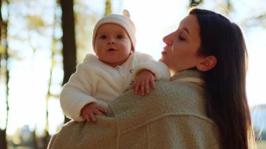 Kızını kollarına alan şefkatli genç bir annenin geçmişe bakışı. Sonbahar parkında güneşli bir günde yürüyen şirin bir ailenin portresi. Açık havada. Huzurlu atmosfer