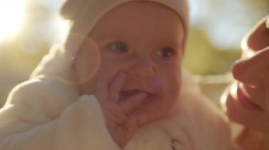 Güneşin altında annesinin kollarında oturan sevimli, gülümseyen bir kızın yakın çekim görüntüleri. Güneşli bir günde anne ve bebek parkta. Doğa. Şefkat, ilgi, aşk konsepti