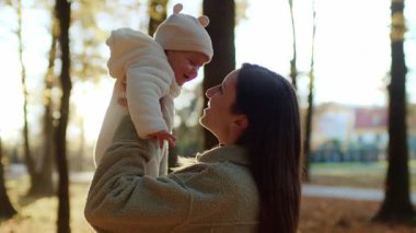 Yumuşak giyimli annenin kucağında bebek resmi. Gülümseyen anne ve bebek sonbahar parkında oynayıp eğleniyorlar. Gün batımında parkın renkli sonbahar manzarası. Doğa. Aile kavramı