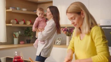 Karısı evde rahat bir mutfakta yemek pişirirken kucağında bebek tutan genç eşcinsel kadın.