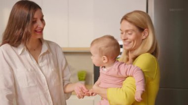 İki gülümseyen anne içeride bebekle konuşup eğleniyor. Lgbt aile kavramı