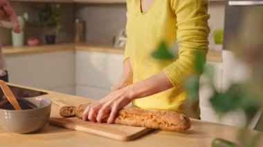 Ekmek doğrayan ve kucağında bebek tutan bir kadın. Lezbiyen çift oğluyla eğleniyor.