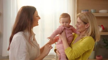 Genç, beyaz, aşık bir kadın pembe elbiseli küçük bir bebeği içeride tutuyor.