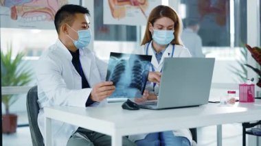 Çok ırklı iki kadın ve erkek doktor Coronavirus akciğer hastalığını tartışıyor ve hastane ofisinde enfeksiyon belirtileri gösteriyor. Yüz maskeleri. Sosyal uzaklık.