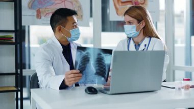 Virüs koruması için yüz maskesi takan çok ırklı bir çift laptopla iletişim kurarak hastalığın tedavisini tartışıyor..