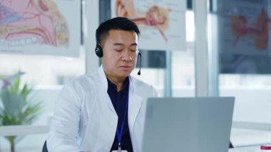 Asyalı sağlık çalışanı genç doktor hastalarla çevrimiçi iletişim kuruyor. Uzaktan görüşmeler, bilgisayarlı bilgisayarlar, ofis hastanesinden tedavi ilaçları..