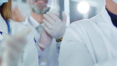 Close-up of multi-national doctors young adults wearing white medical coats, gloves and masks against coronavirus clapping hands on meeting in the office. Hospital staff concept.