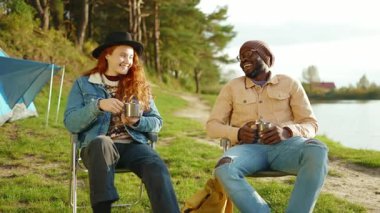 Gün ışığında mutlu adam ve kadın ormanda oturup gülerek çay içerler birbirlerine bakarlar. Seyahat pikniği genç doğa neşeli kamp macerası. Yavaş çekim