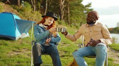 Genç hippi adam ve kadın ormanda oturup çay içerler gülümseyerek birbirlerine bakarlar ve konuşurlar. Seyahat pikniği genç doğa neşeli kamp macerası. Yavaş çekim