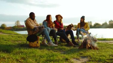 Portre hipster arkadaşları doğada kamp ateşinin yanında oturuyorlar. Gençler oyunlar hakkında konuşurlar, köpeklerin gülümsemesiyle mutlu olurlar. Tatil turizmi macerası. Yavaş çekim