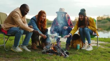 Mutlu arkadaşlar kamp ateşi etrafında oturur ve renkli şekerlemeler kızartırlar. Ormandaki gençler. Kamp yapmak. Piknik. Yavaş çekim
