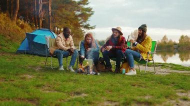 Göl kenarında kamp ateşi etrafında oturmuş renkli şekerlemeler kızartıyorlar. Ormandaki gençler. Kamp yapmak. Piknik. Yavaş çekim