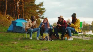 Portre tarzı arkadaşlar kamp ateşi etrafında oturur ve renkli şekerlemeler kızartırlar. Ormandaki gençler. Kamp yapmak. Piknik. Yavaş çekim