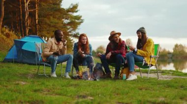 Arkadaşların kamp ateşi etrafında oturup renkli marşmelovları kızartırken rahat ol. Ormandaki gençler. Kamp yapmak. Piknik. Yavaş çekim