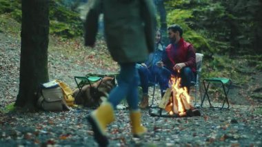 Mutlu aile sonbahar akşamı kamp ateşinin yanında oturur. Ebeveynleriyle birlikte çocuklar ormanda dinleniyorlar. Çocukluk ilişkisi kamp kuruyor. Kapatın. Yavaş çekim