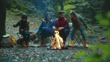 Portre ailesi sonbahar akşamı kamp ateşinin etrafında oturur. Ebeveynleriyle birlikte çocuklar ormanda dinleniyorlar. Çocukluk ilişkisi kamp kuruyor. Kapatın. Yavaş çekim