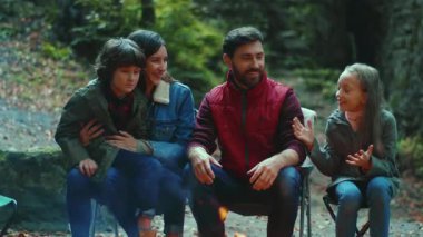 Mutlu aile sonbaharda kamp ateşinin yanında oturur. Ebeveynleriyle birlikte çocuklar ormanda dinleniyorlar. Çocukluk ilişkisi kamp kuruyor. Kapatın. Yavaş çekim