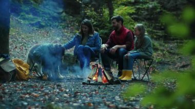 Mutlu aile sonbaharda kamp ateşinin etrafında oturur. Ebeveynleriyle birlikte çocuklar ormanda dinleniyorlar. Çocukluk ilişkisi kamp kuruyor. Kapatın. Yavaş çekim