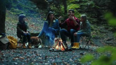 Ağır çekim ailesi sonbaharda kamp ateşinin yanında oturup konuşur. Ebeveynleriyle birlikte çocuklar ormanda dinleniyorlar. Çocukluk ilişkisi kamp kuruyor. Kapat.
