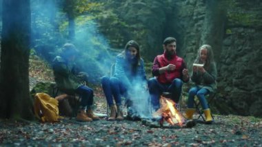 Mutlu aile, sonbahar ormanlarında kamp ateşinin yanında oturup yemek yer. Ebeveynleriyle birlikte çocuklar ormanda dinleniyorlar. Çocukluk ilişkisi kamp kuruyor. Kapatın. Yavaş çekim