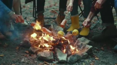 Yakın aile, sonbahar akşamı ormanda kamp ateşinin etrafında oturur. Ormandaki bir yangında sosis kızartmak. Dostluk mutluluğu şömineyi pişirir. Yavaş çekim