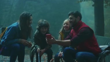 Köpekli bir aile, sonbahar akşamı ormanda kamp ateşinin etrafında oturur. Ormandaki bir yangında sosis kızartmak. Telefonu kullan. Arkadaşlık şömineyi pişirir. Kapatın. Yavaş çekim