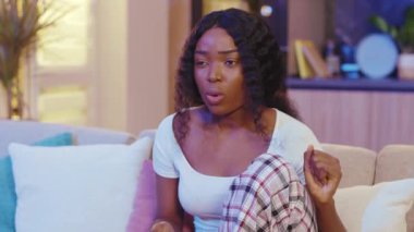 Karanlık oturma odasındaki koltukta oturan korkmuş Afrikalı Amerikalı kadın. Geceleri televizyon izlerken uzaktan kumandayla kanal değiştirmek. Yavaş çekim