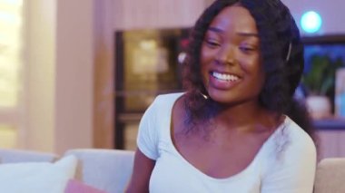 Gülen suratlı, kulaklıklı, iletişim kuran, bilgisayar kullanan Afro-Amerikan kadın. Evde video var. Mesafe ilişkisi. Yavaş çekim