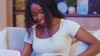 Rahat Afro-Amerikan kadın evde kedisiyle kanepede oturmuş dijital tablet bilgisayar kullanarak gülümsüyor. Görüntülü arama. Yavaş çekim