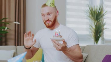 Çekici bir adam evdeki kanepede oturmuş gülümsüyor dizüstü bilgisayarla pastadaki mumları üflüyor. Karantina sırasında online video görüşmesinde doğum gününü kutluyoruz. İletişim. Kapatın. Yavaş çekim