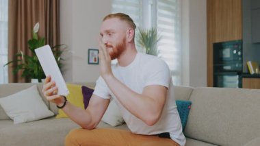 Gün ışığında tablet bilgisayar kullanan yakışıklı bir adam. Evdeki kanepede oturmak. Çevrimiçi teknoloji cihazı iletişim karantinası. Yavaş çekim