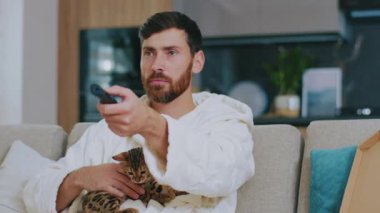 Kedisi olan hassas bir adam televizyon izliyor. Kanepede oturup evde hüzünle ağlamak. Dinlenme sinema kanalları dinleniyor. Portre. Kapatın. Yavaş çekim.