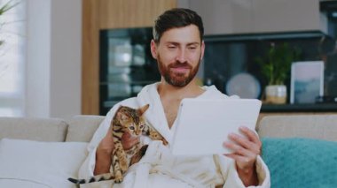 Evde kedisi olan yakışıklı bir adam arkadaşıyla görüntülü konuşma yapıyor. Evde kal. İletişim konferansı sosyal medya portresi. Yavaş çekim