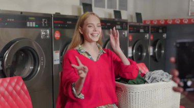 Kapalı ellerde telefon var. Arka planda sarışın bir kadın var. Çamaşır odasında oturmuş müzik pozları dinliyor. Ev işi çamaşır makinesi kurutma makinesi içeride. Kapatın. Yavaş çekim